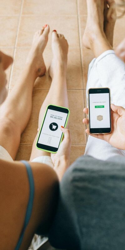 A couple using smartphones for online shopping while relaxing indoors on a tiled floor.