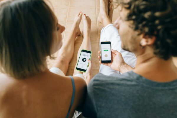 A couple using smartphones for online shopping while relaxing indoors on a tiled floor.