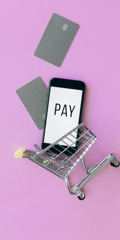 Top view of a smartphone in a shopping cart with credit cards on a purple background.